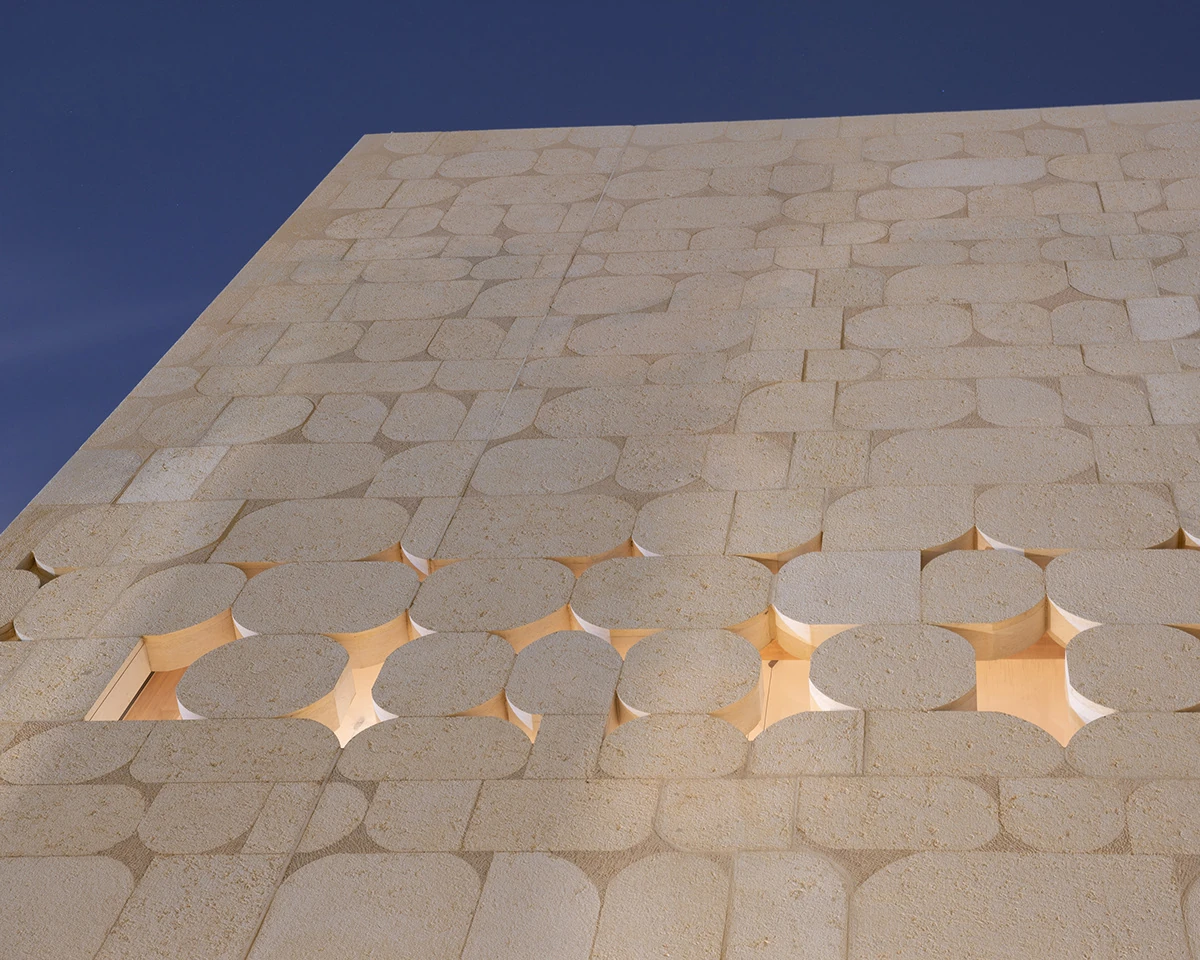 Sunlight through geometric openings in the stone facade
