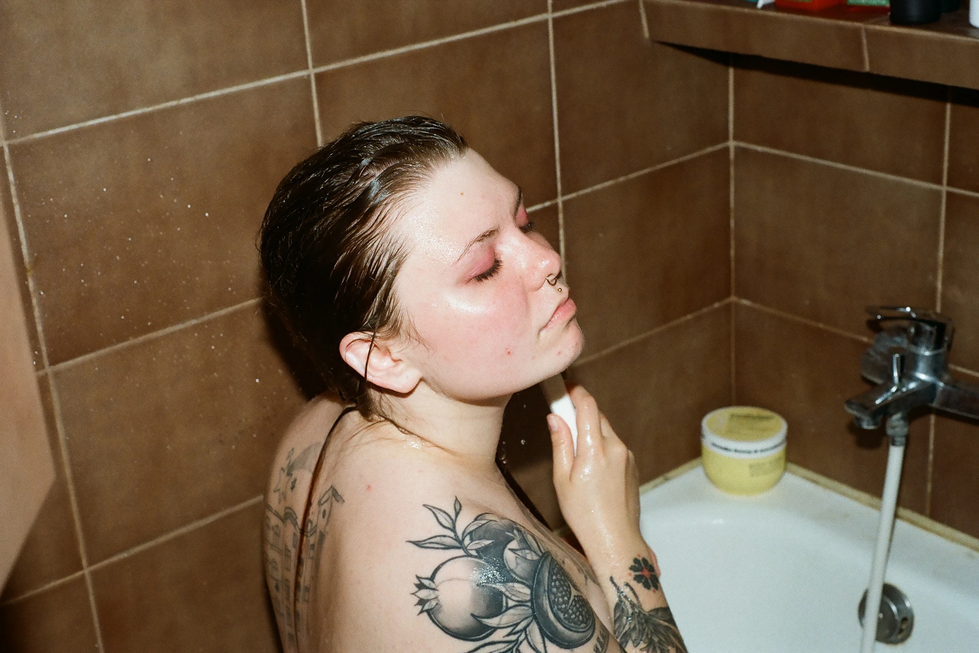 A tattooed person sitting beside a tiled bath
